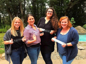 Four people smiling and standing outside. Each person is holding a transparent name placard.